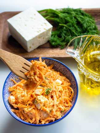 Creamy Shredded Carrot Salad in a bowl alongside olive oil, feta cheese and fresh dill