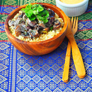 Quinoa Mushroom Salad in a wooden bowl alongside wooden utensils and sauce