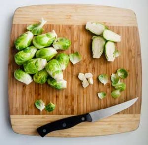 Trimmed and Halved Brussels Sprouts on a cutting board alongside knife